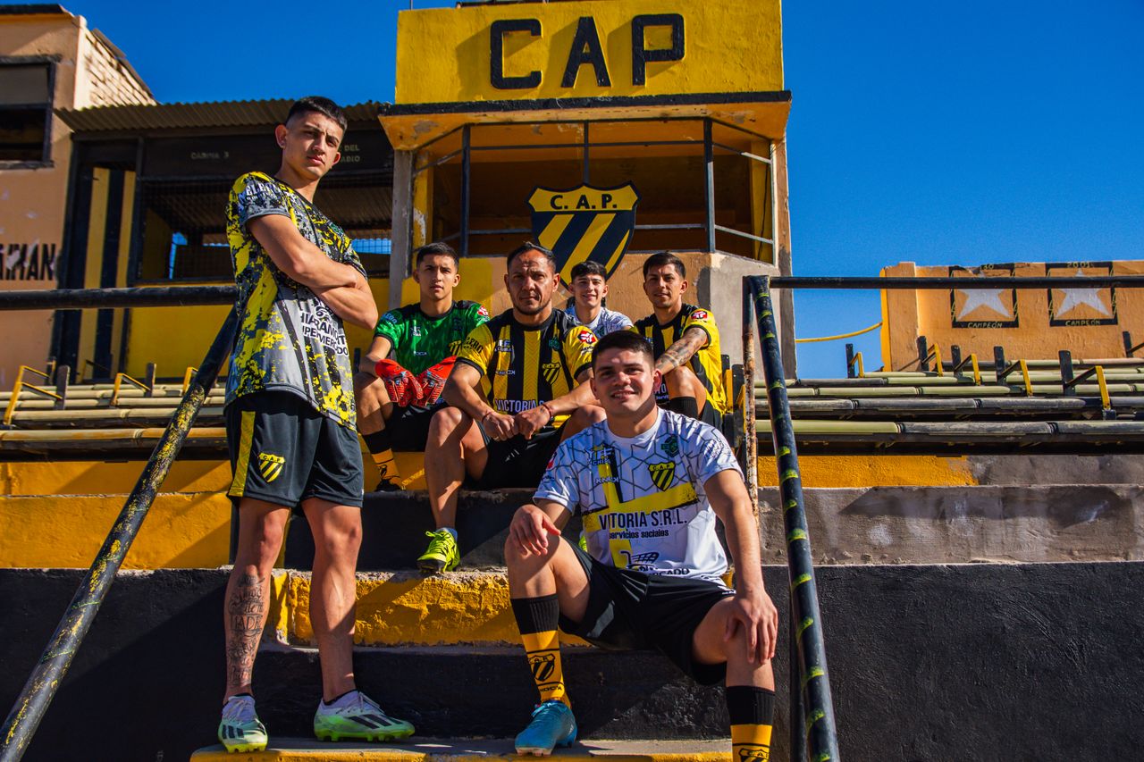 A soccer team dressed in yellow and black jerseys posing confidently at the CAP Stadium under a clear blue sky.